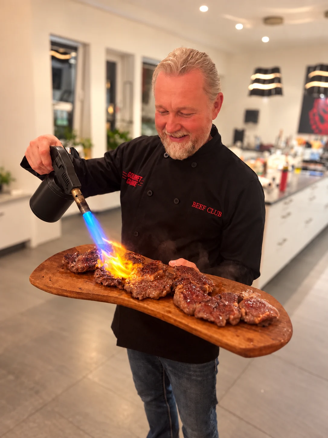 Robert Jäger flambiert Steaks auf einem Holzbrett mit einem Bunsenbrenner